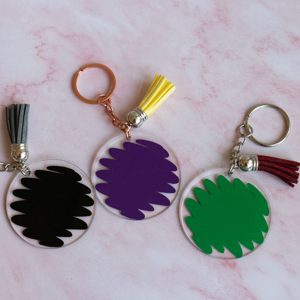 Three colorful keychains with scribble designs on a pink marble background