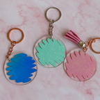 Three colorful keychains with scribble designs on a pink marble background